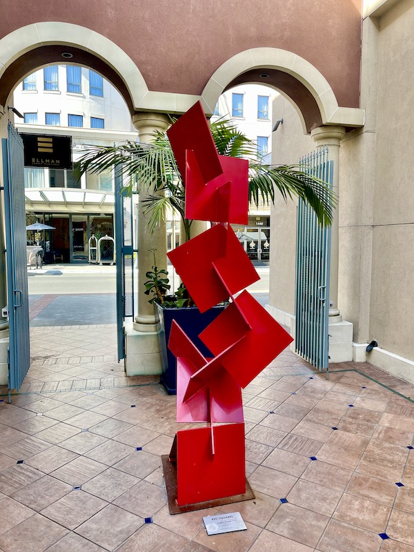 Red metal and paint sculpture of squares sitting on terra cotta pavers in a courtyard, see while having Fun in Downtown Napa CA