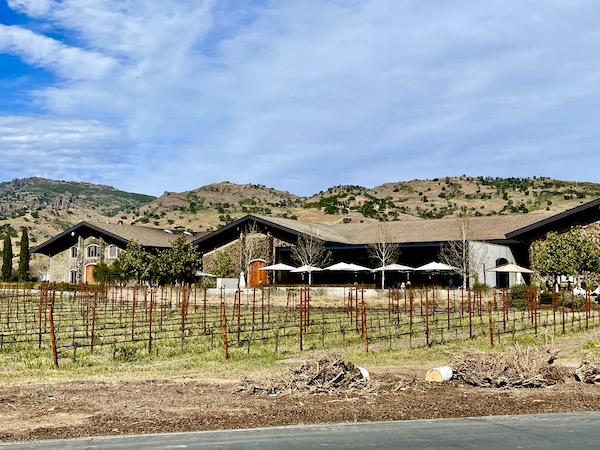 Ranch style stone building with mountains and vineyard on our Napa Valley Winery Tour