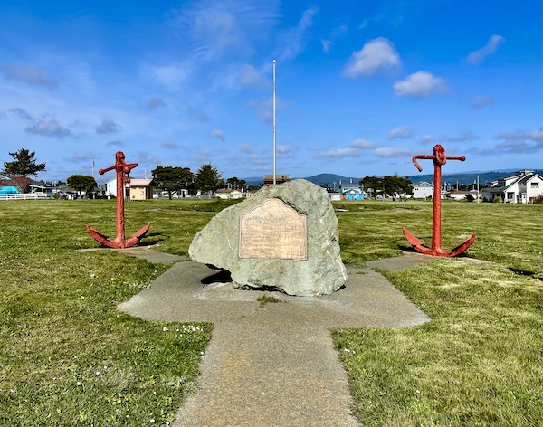 A large rock with a brass plaque flanked by two anchors in Crescent City California