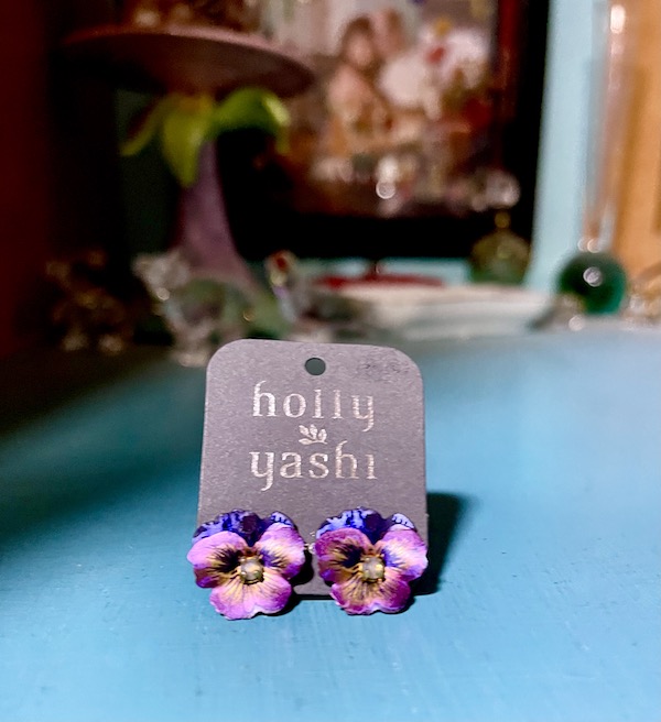 A gray earring card holding a pair of purple pansy earrings from the Holly Yashi Store and Studio