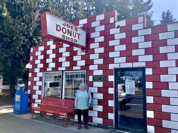 A silver haired woman in a light green hoodie in front of a red and white brick building on the way to Mt. Hood Oregon