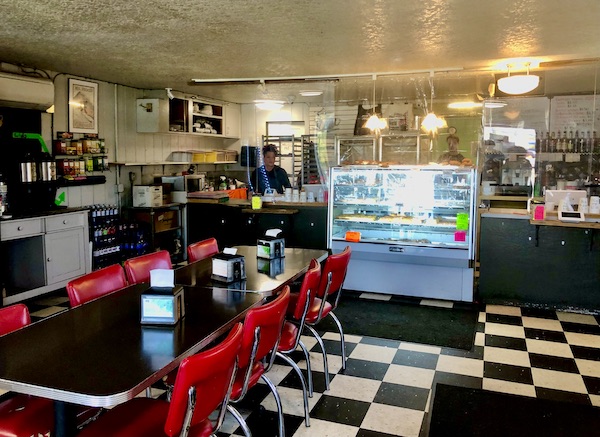 Inside a donut shop with pastry cases, counters, black and white floor, black table and red chairs