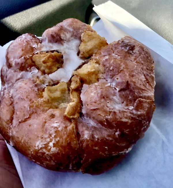 An apple fritter with lots of apples sitting on a piece of white deli paper