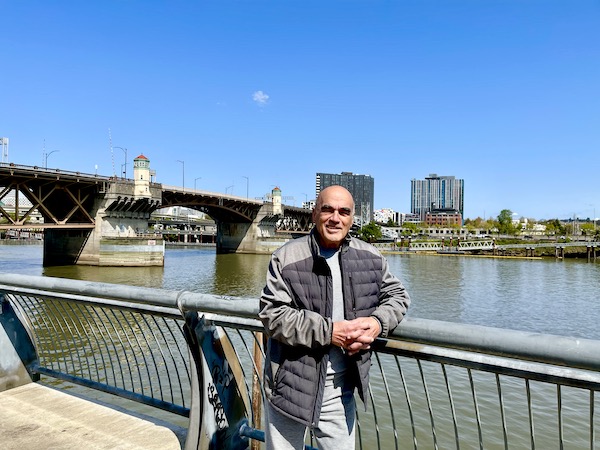 A man in a gray jacket leaning on the railing by a river.