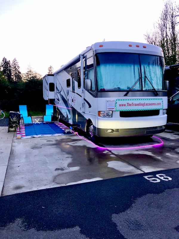 A white and tan RV set up with lights and turquoise chairs near Multnomah Falls Oregon