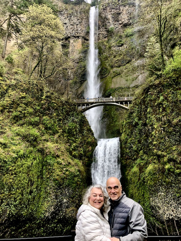 A couple standing in front of a two tiered waterfall known as Multnomah Falls Oregon