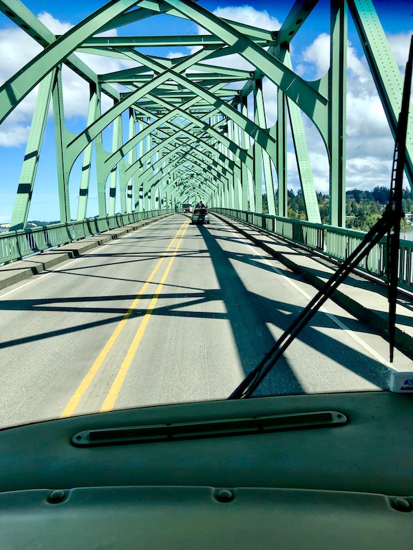 A paved bridge with solid double yellow lines up the middle and green metal grid overhead on our way to Multnomah Falls Oregon