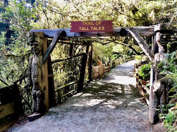 Entry to a trail with a brown sign that reads Trail of Tall Tales at Trees of Mystery Klamath CA