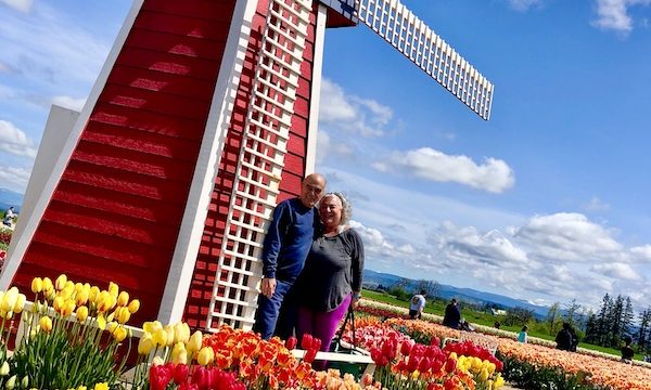 A loving couple at a red windmill and colorful flowers at the Wooden Shoe Tulip Festival Oregon