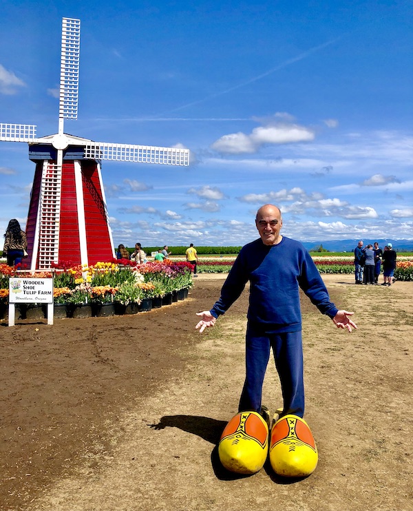 A red and white windmill and a man standing in an oversized pair of yellow wooden shoes.