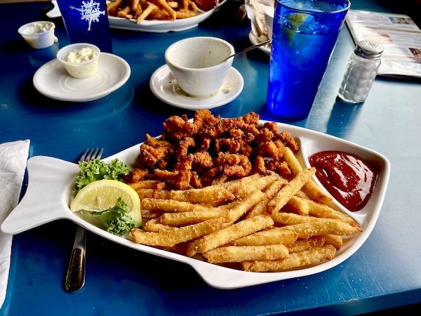 A fish shaped white plate topped with French Fries, fried clam strips, lemon wedge and cocktail sauce in Cannon Beach Oregon