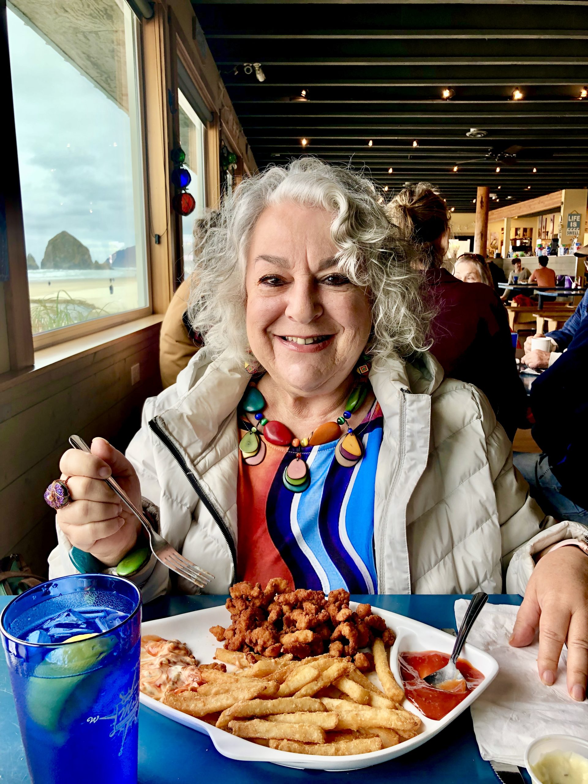 A silver haired woman in a gray jacket eating a seafood lunch in Cannon Beach Oregon