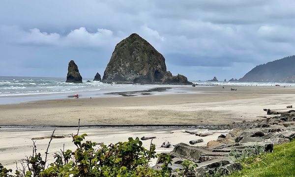 A large rock jutting out of the ocean and sandy beach in Cannon Beach Oregon