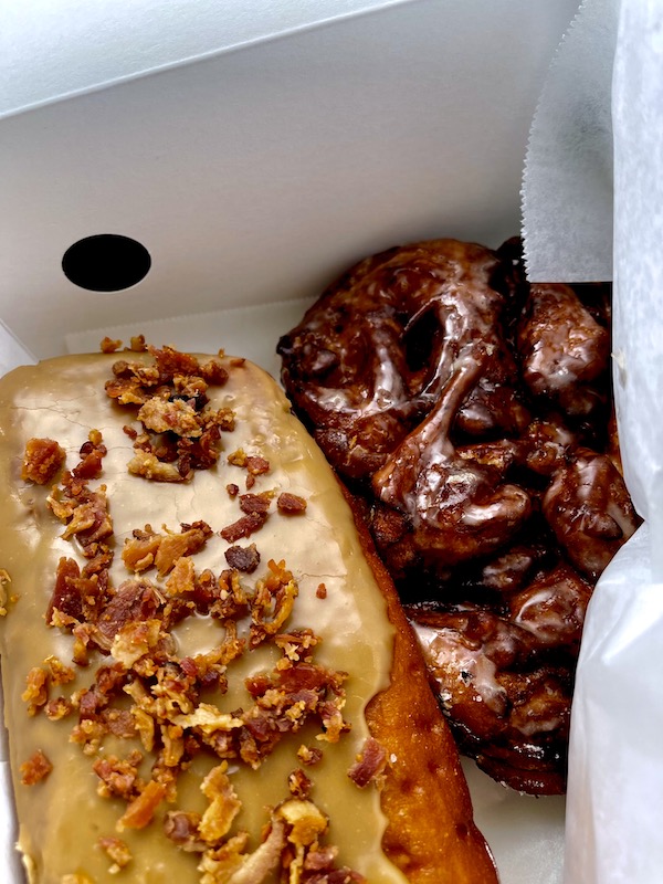 Inside a white box is a maple and bacon topped donut bar and an apple fritter from Legendary Doughnuts Tacoma WA
