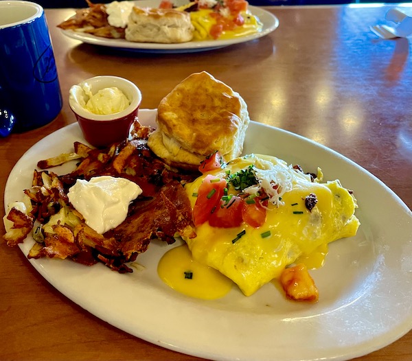 A plate at a diner topped with an omelet, hash brown potatoes, sour cream, butter in a cup and a biscuit.