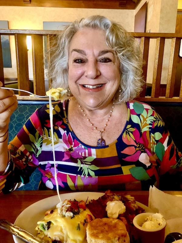 A woman eating a cheese omelet with the cheese stretching from plate to fork.