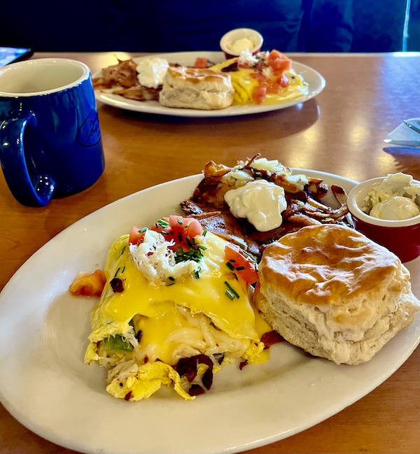 An off-white oval plate topped with a cheesy omelet, biscuit and home fries at a restaurant