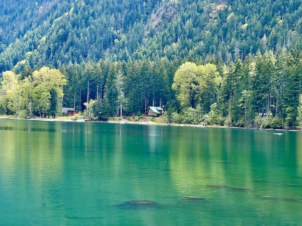 Emerald green lake water, mountains and trees are a background for a cabin in the Olympic Peninsula Washington