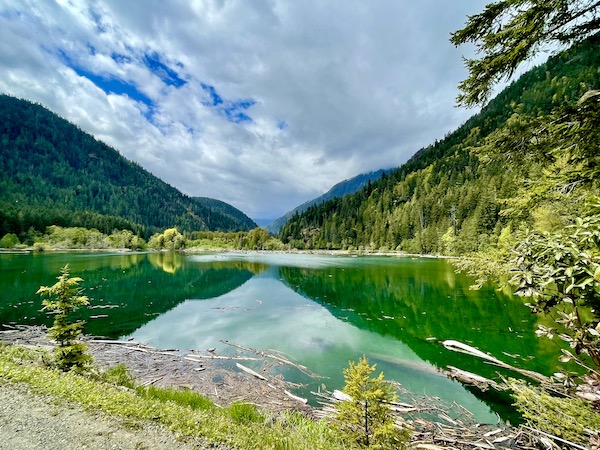 Green lake water, mountains, trees and blue sky peaking through clouds in the Olympic Peninsula Washington