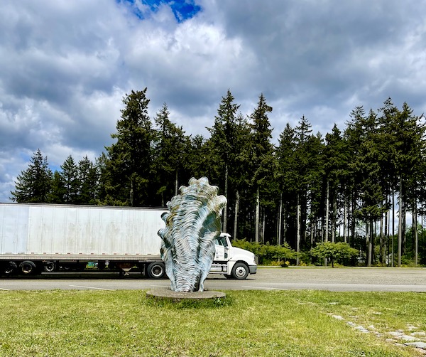 Large oyster shell sculpture, large white semi truck, lawn and trees in Olympic Peninsula Washington
