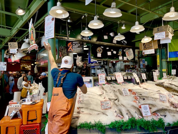 A fish stand with a fish flying through the air to a waiting fish monger in orange coveralls at Pike Place Market Seattle WA