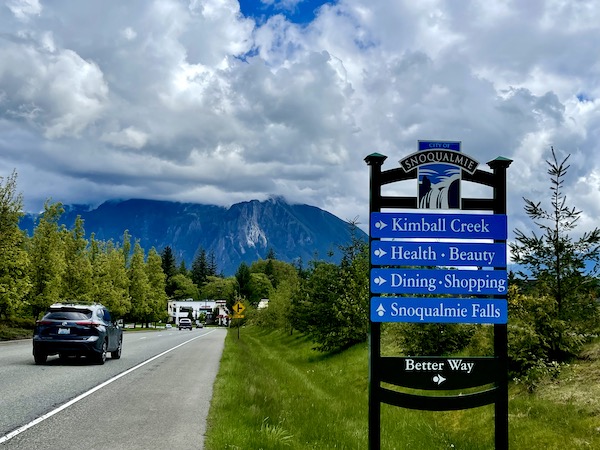 Cars on a highway, lawn trees and mountains en route to Snoqualmie Falls Washington