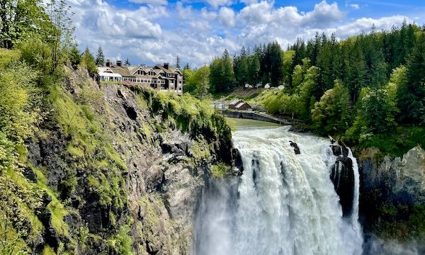Powerful waterfall with rocks trees houses and blue sky at Snoqualmie Falls Washington