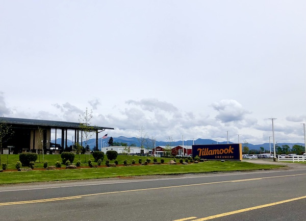 Part of building, sign and parking lot with mountains in the backgrounds where we came for our Tillamook Cheese Factory Tour