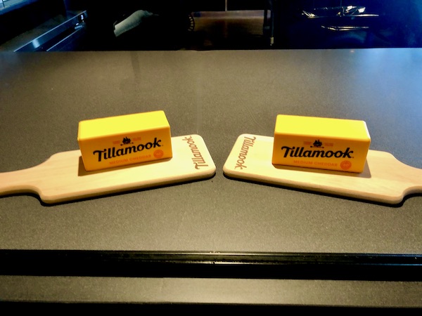 Two cutting boards each topped with a bright yellow wrapped block of Tillamook cheese