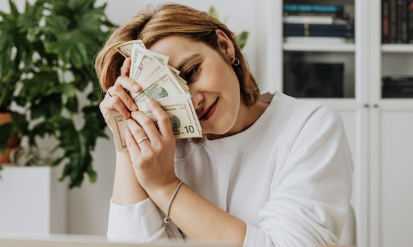 Woman holding money while sitting at the computer learning easy ways to make money while you travel