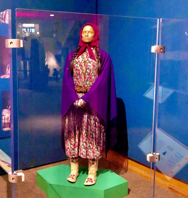 Multicolor print dress on mannequin covered by purple fringed shawl, red head scarf and wearing leather boots