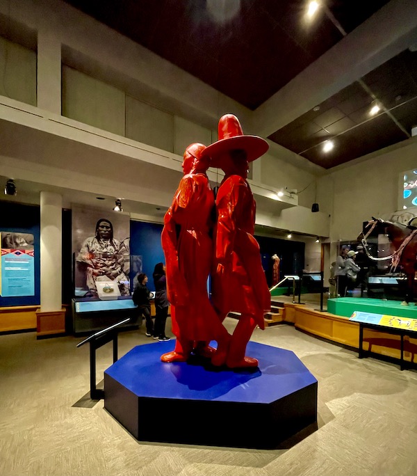 Red sculpture of a native American man and woman back to back.