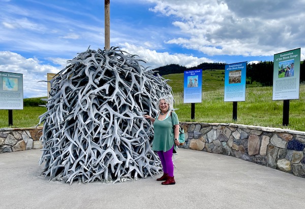 A woman standing next to a pole piled high with elk antlers.