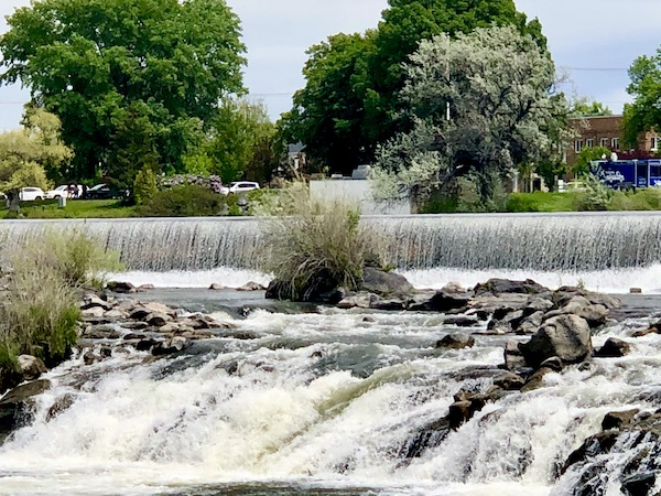Water rushes over rocks with Idaho Falls in background
