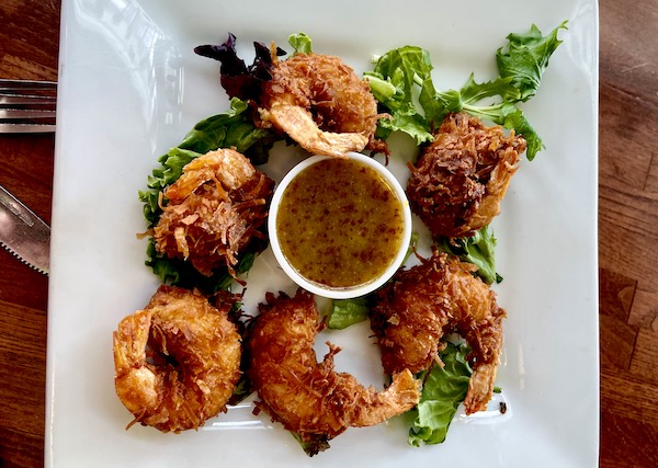 White plate with coconut shrimp, greens and a dipping sauce in a restaurant in Idaho Falls
