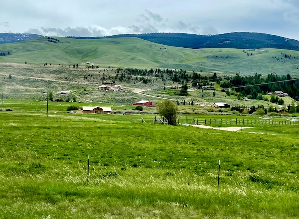 Rolling green pasture and red barns with Teton Mountain Range Wyoming in background
