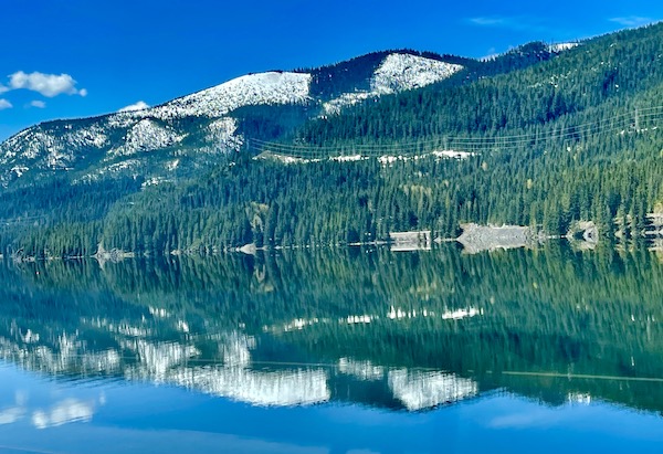 Snow capped mountains and trees reflected in very still lake on our way to Visiting Spokane Washington