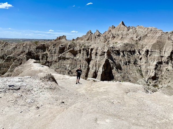 Steve, in black tee and shorts looking very small compared to the rock formations at Badlands NP.
