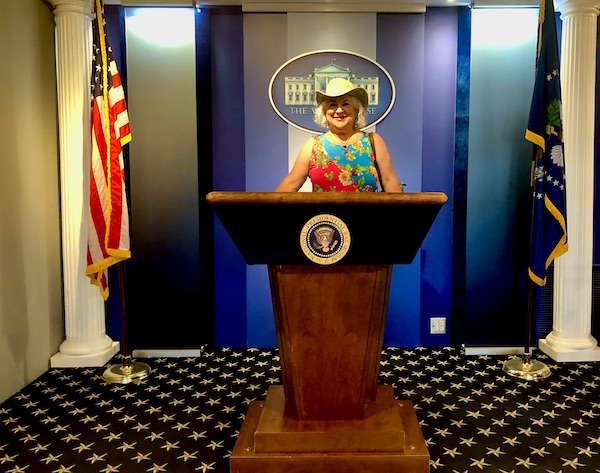 Me in a print dress and pale green cowboy hat at the White House podium in the National Presidential Wax Museum Keystone SD