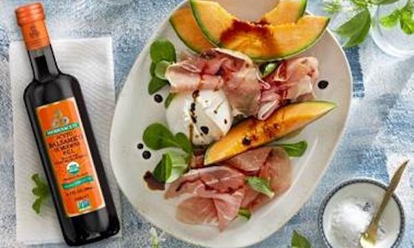 White plate with ham, cheese and cantaloupe sitting next to a bottle of balsamic vinegar with an orange label, part of my 2022 Holiday Gift Guide