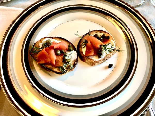 Two canapés of smoked salmon, cream cheese and capers on a black rimmed plate.