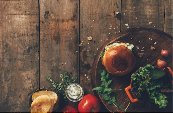 Another easy way to expand your palate is this burger with veggies and toppings on a wood cutting board