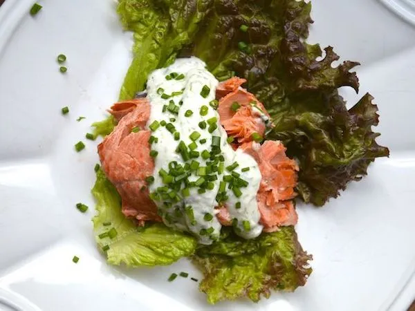 Poached salmon with dill horseradish sauce sitting on lettuce leaves atop a white plate as another way for Incorporating Seafood into Your Social Occasions