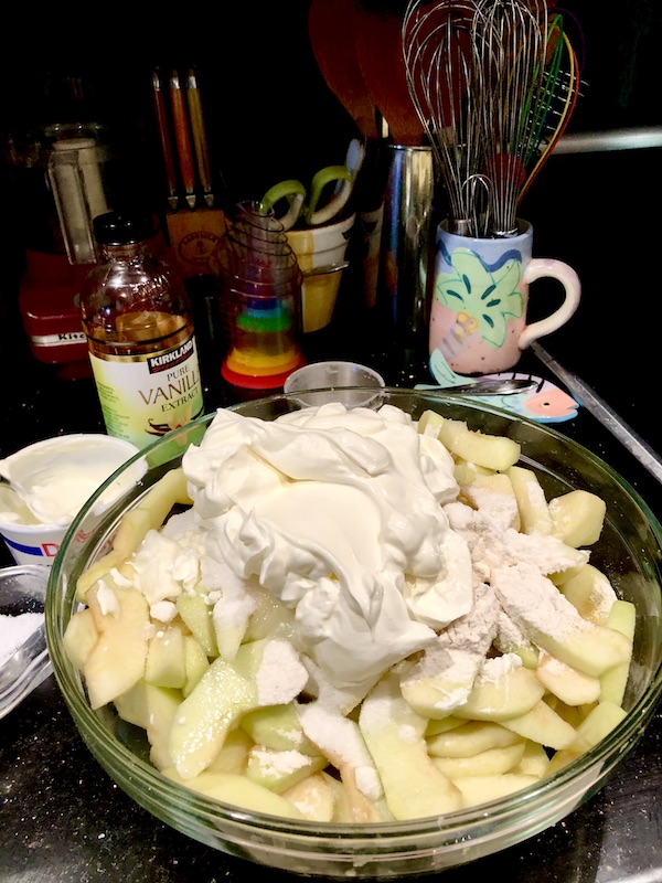 Glass bowl filled with sliced apples, sour cream and additional ingredients for Candied Apple Walnut Pie