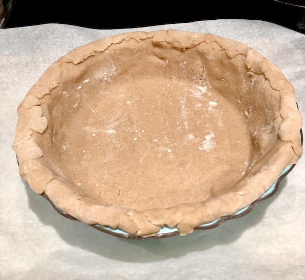 Pie shell in aqua deep dish pie pan sitting on parchment paper for Candied Apple Walnut Pie