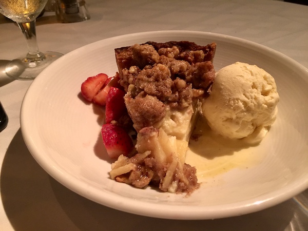 White plate topped with slice of Candied Apple Walnut Pie sliced strawberries and scoop of vanilla ice cream.