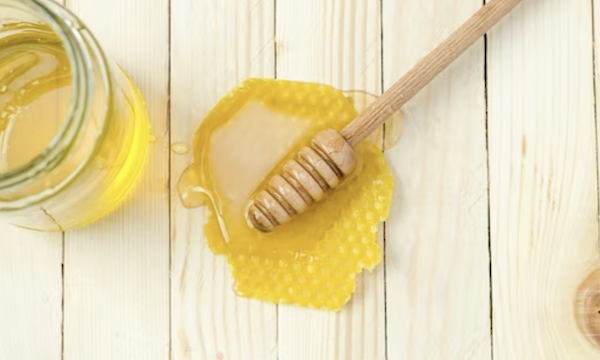 Puddle of honey on a white board table with honey server to highlight the Importance of choosing organic honey