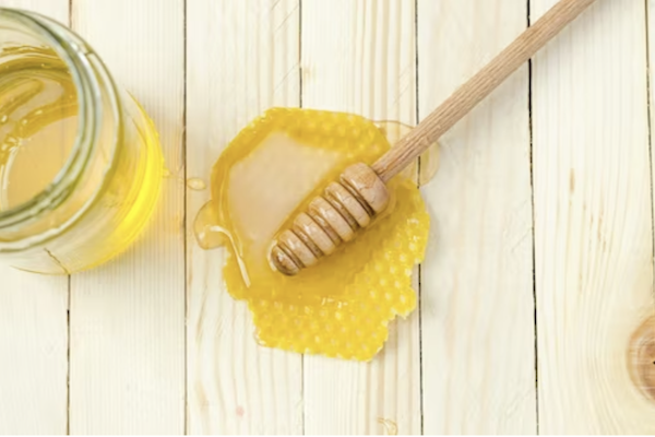 Puddle of honey on a white board table with honey server to highlight the Importance of choosing organic honey