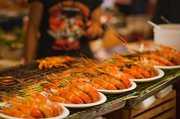 A row of white plates each topped with 4 cooked head on shrimp as an idea of Incorporating Seafood into Your Social Occasions