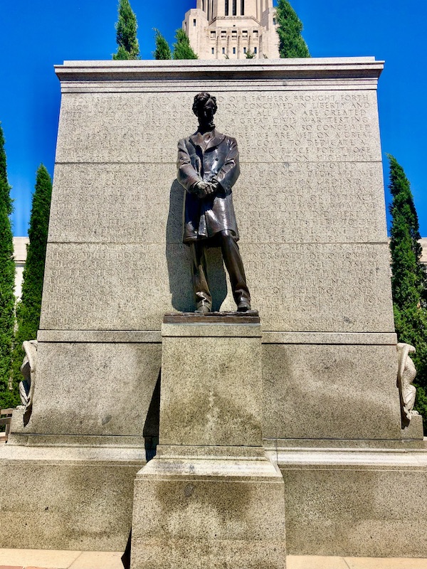 Bronze statue of Abraham Lincoln on concrete pedestal with Gettysburg Address engraved in wall behind statue at the Nebraska State Capitol in Lincoln